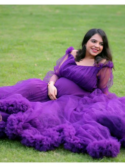 An outdoor shot of a mother-to-be seated on the grass, surrounded by the voluminous ruffles of her purple gown. This shows how we take our glamorous gowns outdoors for a fairytale look.