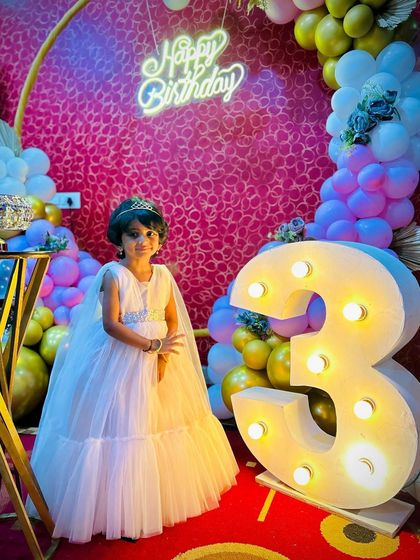The birthday princess posing for a photo. The combination of the large marquee number, colorful balloons, and neon sign creates a fantastic and memorable birthday picture.