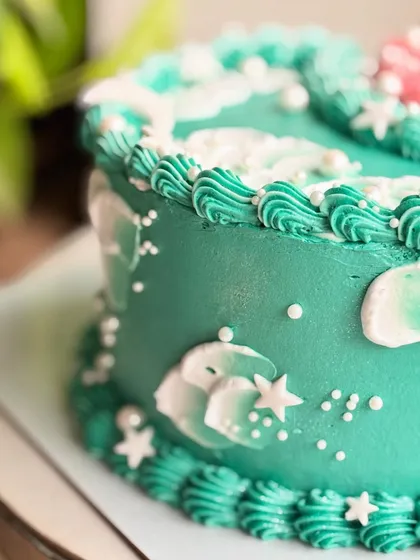 A close-up of the moon side of the cosmic cake, showing the detailed piping, stars, and clouds.