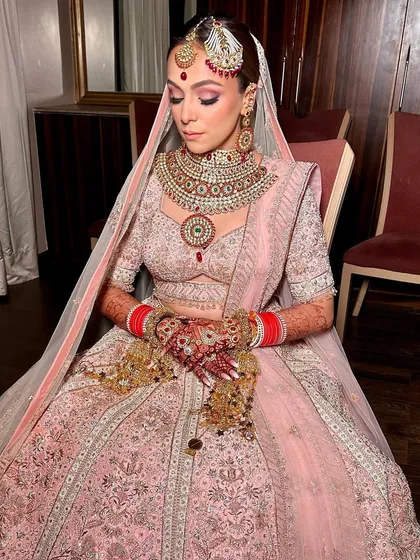 A serene moment captured, showing the bride's complete look. Her dewy makeup, combined with the soft pastel lehenga and traditional jewelry, creates an aura of timeless elegance.