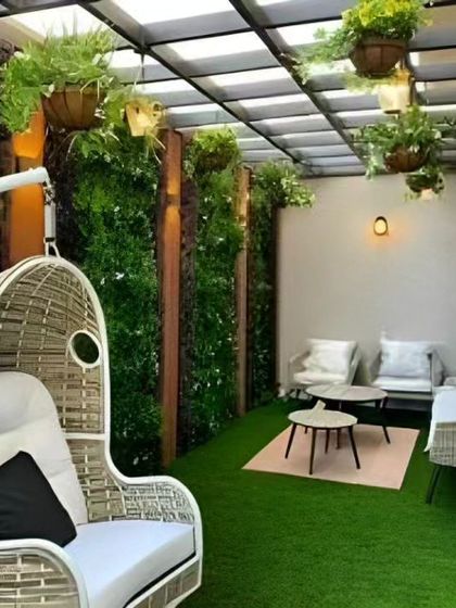 A cozy balcony setup with a wicker swing chair and a vertical garden. The artificial grass flooring adds a touch of green and is easy to maintain, perfect for a city apartment.