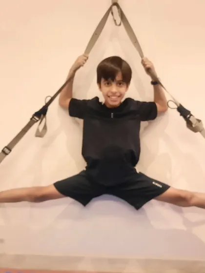 We use safe and effective tools to achieve amazing results. Here, a student uses suspension straps for an assisted wall split, a technique that helps deepen the stretch and build strength in a full range of motion.