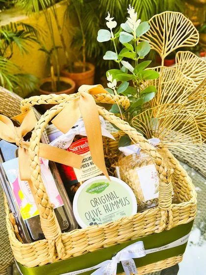 This Sicily-themed custom birthday hamper incorporates Mediterranean elements. It includes olive hummus, Sicilian spiced nuts, and other gourmet items in a beautiful handwoven basket with elegant green accents.