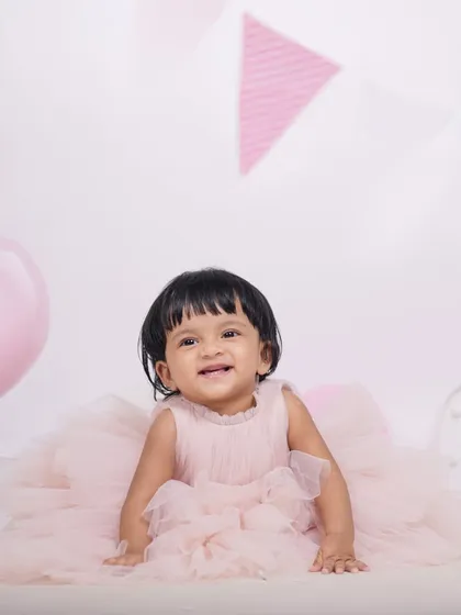 Capturing the happy expressions of a baby girl during her first birthday studio photoshoot. The soft pink theme with balloons and banners creates a lovely, celebratory mood.