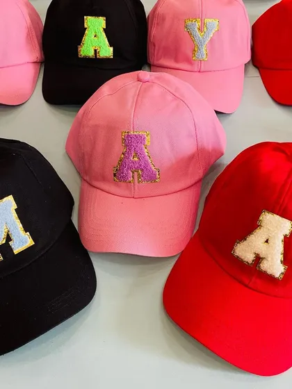 A display of our custom initial caps in red, pink, and black, showing the vibrant and fun options available for personalizing party gifts.