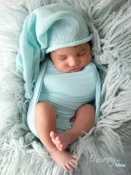 Swaddled snugly in a soft blue wrap and a sleepy hat. This classic newborn pose emphasizes how tiny and peaceful they are in their first few weeks.