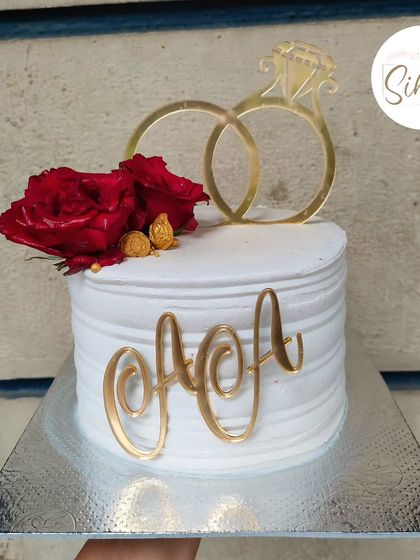 Roses and rings are a classic combination for an engagement. This simple white cake features a textured finish, a gold ring topper, and a beautiful fresh red rose.