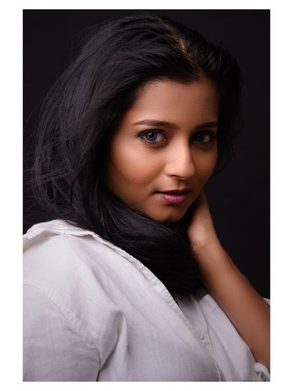 A simple and beautiful headshot with a clean, dark background. The wind in her hair adds a dynamic element, while her direct gaze creates a strong connection with the viewer.