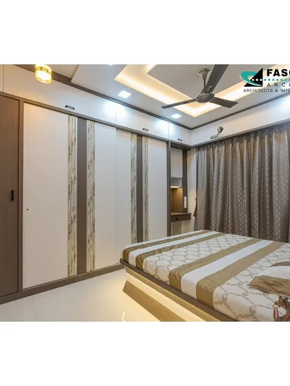 A full view of a bedroom in Bhiwandi, showing the complete wardrobe unit and bed. The design uses a consistent palette of neutral colors and wood textures for a harmonious and restful feel.
