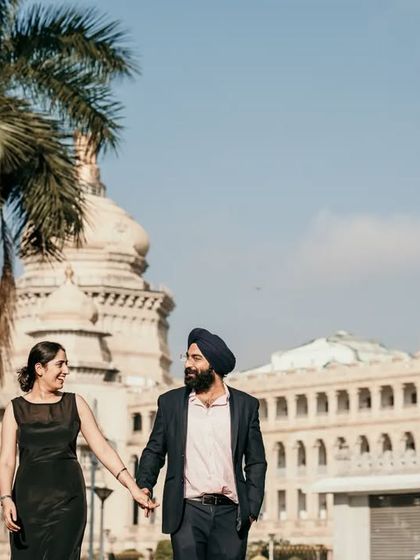 A duplicate of image 73, a couple walks hand-in-hand with an iconic Bangalore building behind them.