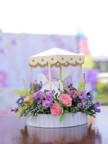An elegant miniature carousel centerpiece with fresh flowers. This detail is perfect for adding a sophisticated touch to a whimsical carnival-themed table setting.