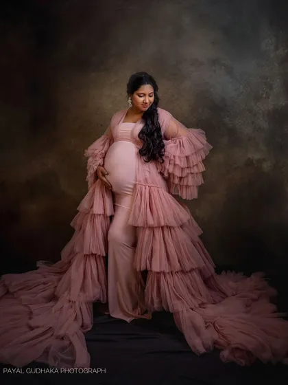 A full-length portrait against a textured, dark backdrop. The mom-to-be looks down at her bump, creating a quiet and contemplative mood.