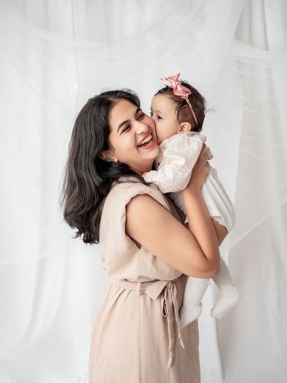 A mother getting a sweet kiss on the cheek from her baby girl.