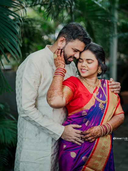 A tender moment captured in a lush, green setting. The groom gently holds the bride's face as they share an intimate embrace, showcasing their deep connection.