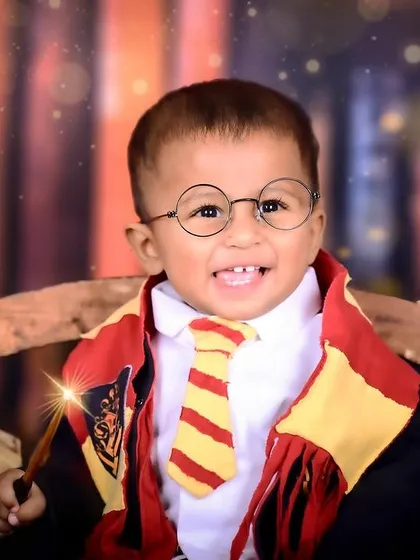 A smiling baby dressed as Harry Potter, with a magic wand creating a spark effect.