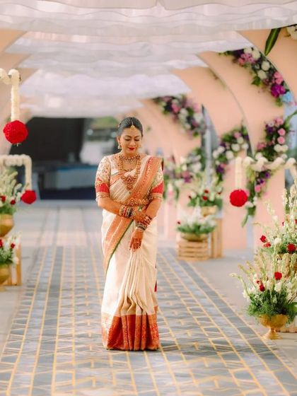 A grand entrance for a beautiful bride. Her custom puff-sleeve blouse adds a touch of traditional charm to her classic white and red wedding saree.