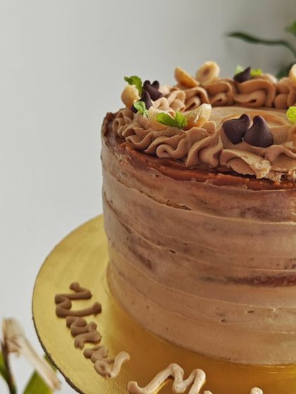 A side view of the vanilla and Biscoff cake, showing the rustic textured frosting and the personalized message written on the cake board.