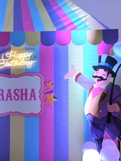 A close-up of the main circus tent backdrop, featuring a neon 'Happy Birthday' sign and a personalized nameplate for the birthday girl, Prasha.