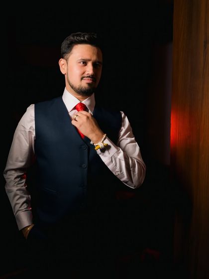 A classic groom portrait using low-key lighting. The focused light on his face and red tie creates a bold, confident, and sophisticated look.