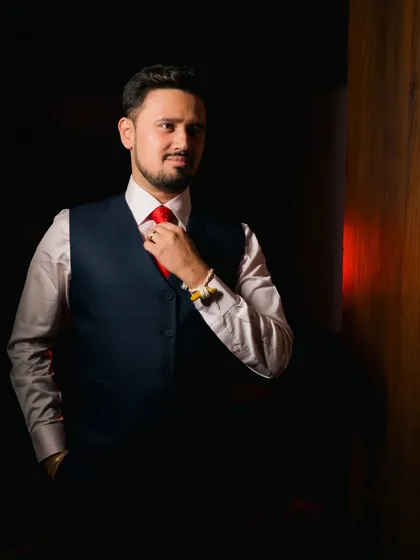 A groom getting ready, adjusting his red tie, with dramatic lighting creating a sense of anticipation.