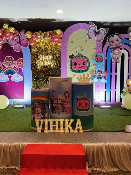An elaborate Cocomelon themed stage setup for a first birthday. This decoration features multiple arched backdrops with characters, a faux grass floor, and a colorful balloon arrangement with butterfly accents.