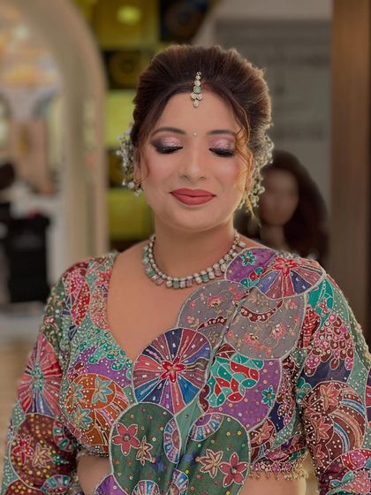 A beautiful party look featuring a colorful, artistic blouse. The makeup is soft and glamorous, with shimmery lilac eyeshadow and a matching lip color.