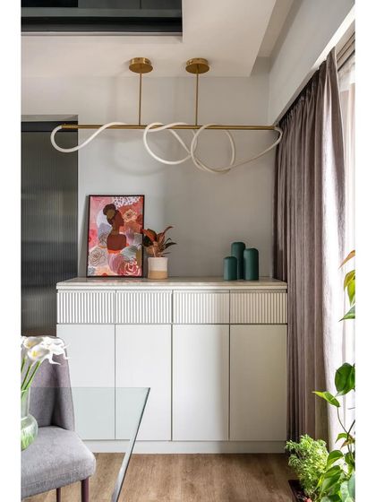 This elegant crockery unit features clean white lines, fluted detailing, and a modern sculptural light fixture. It provides ample storage while serving as a beautiful decorative element in the dining area.