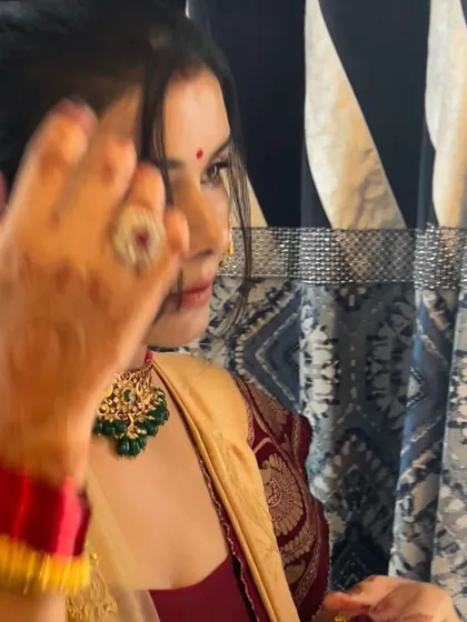 A candid, slightly blurred shot that captures the beautiful motion and emotion of getting ready. You can still see the sparkle of the green beaded choker and the intricate henna design on her hand.