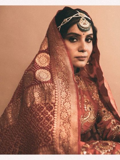 The bride's gaze, framed by a traditional bandhani dupatta. The rich red and gold tones of her outfit are a classic choice, styled here with a vintage aesthetic for a look that is both regal and deeply personal.