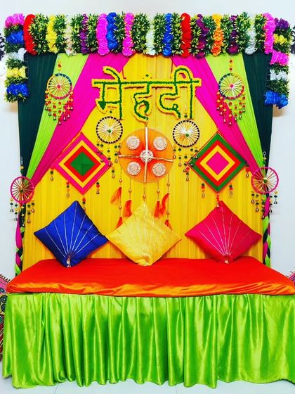A beautiful Mehendi stage setup in Rohini, featuring a comfortable divan, colourful cushions, and a vibrant backdrop with traditional decor.