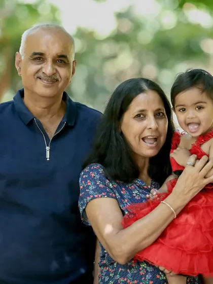 Grandparents smiling brightly as they hold their grandchild during an outdoor family photoshoot.