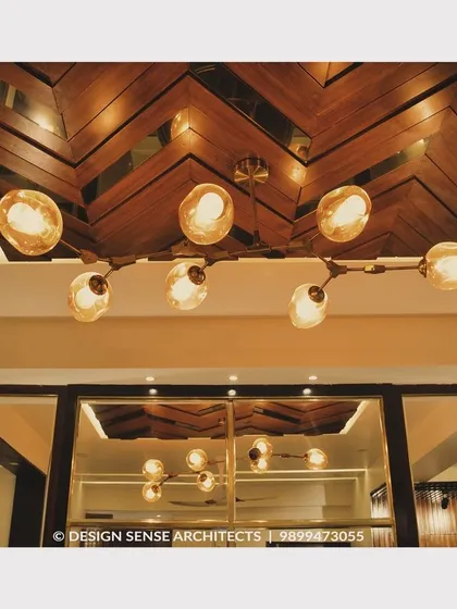 A stunning ceiling detail featuring a herringbone pattern in wood veneer, complemented by a modern, branching light fixture with globe bulbs.