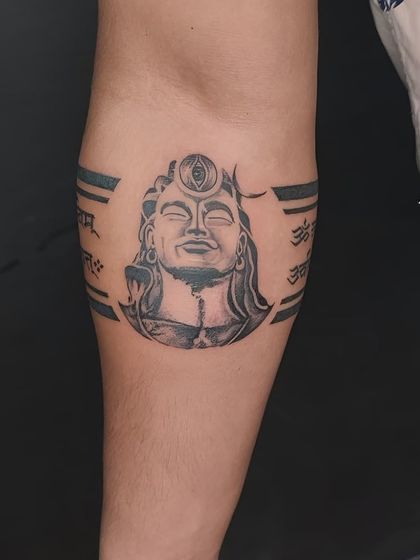 A Shiva-themed armband tattoo. This design features a portrait of a meditative Shiva with his third eye, perfect for a wrap-around forearm piece.