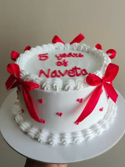 A classic anniversary cake design with red ribbons and piped details, celebrating "5 years of Naveta."