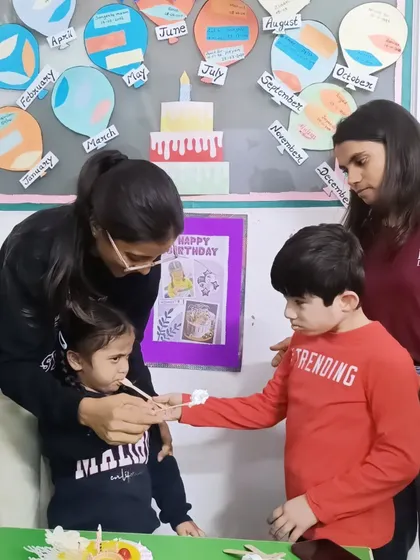A teacher helps a child share a piece of birthday cake with a friend. This simple act teaches generosity and social interaction.