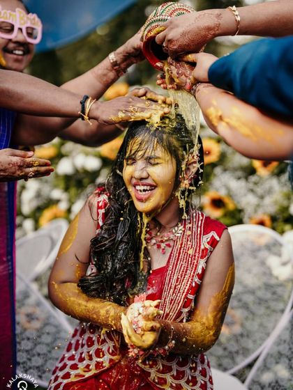 A joyful shot of the bride getting showered with turmeric and water during her Haldi.