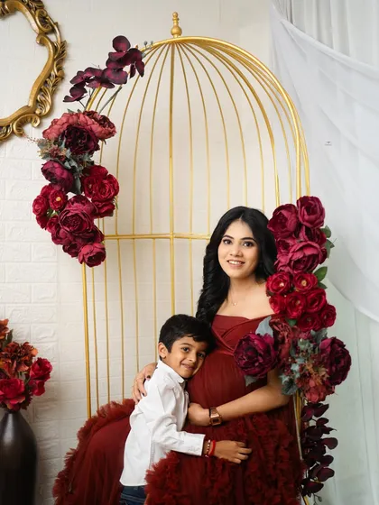 A mother and her son share a special moment during a maternity session. This portrait, with its rich red tones and elegant props, shows how I love to include older siblings in celebrating the coming arrival.