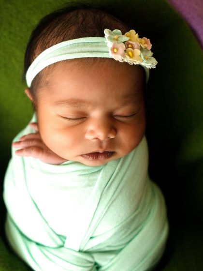 A detailed close-up of a newborn's face, showing her peaceful expression while swaddled in a mint green wrap.