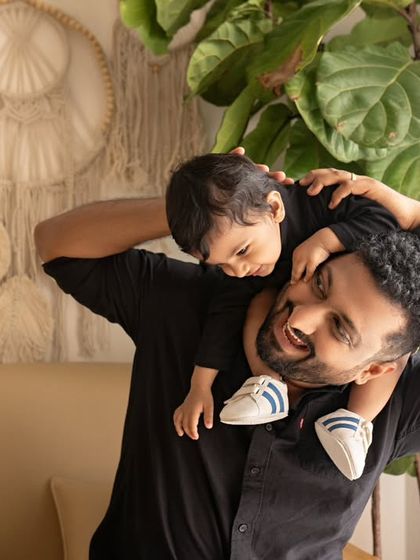 A father holds his son on his shoulders, both of them happy and smiling.