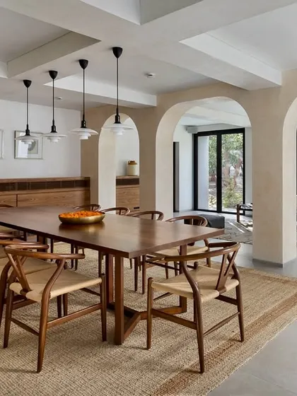 Arched openings and a long wooden dining table create a sense of communal warmth in the Mango Orchard House. The design blends traditional architectural elements with modern simplicity, resulting in a timeless dining space.
