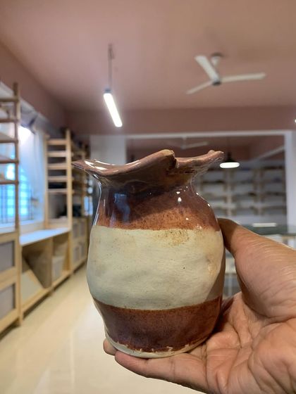 A beautiful two-toned vase with a ruffled rim, held up in our studio. This piece was created by a young student, showcasing their natural talent for form and color.