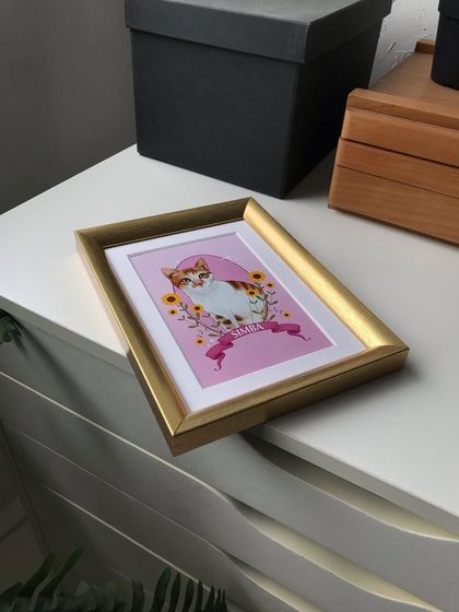 Simba's framed portrait resting on a white drawer unit in my studio. The gold frame contrasts nicely with the modern, minimal furniture.