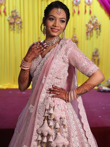 A close-up of a bride in a pink lehenga, showing the detailed craftsmanship of the blouse and the elegant tassels on the skirt.