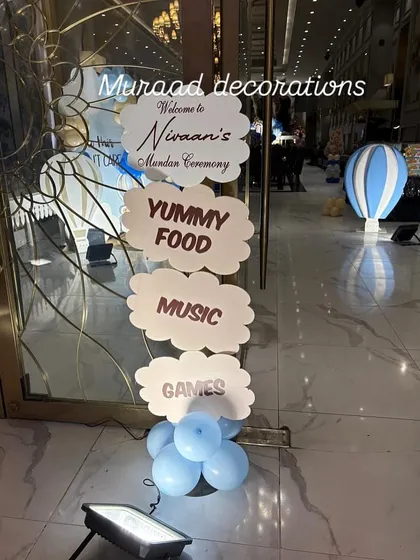 A fun and informative welcome sign for Nivaan's Mundan ceremony. The cloud-shaped signs guide guests to the 'Yummy Food, Music, and Games', setting a playful tone right from the entrance.