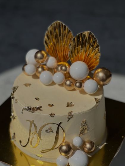 An elegant white and gold cake perfect for an engagement or anniversary. It features gold leaf accents, delicate gold and white spheres, and fan-like toppers for a touch of art deco glamour.