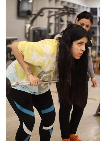 A female trainer guides another member through a bent-over row, showcasing our commitment to one-on-one support and proper technique.