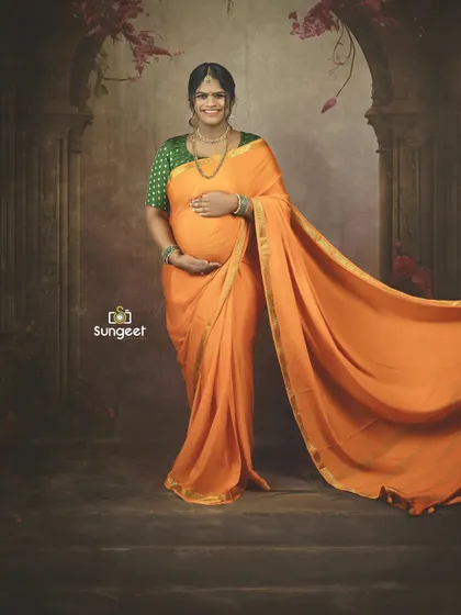 A joyful standing portrait, where the flowing orange saree adds a sense of movement and vibrancy to the maternity photo.