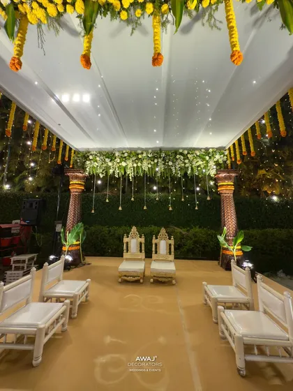 A close-up of the mandap seating, with traditional chairs for the bride and groom set under a canopy of white and yellow flowers.