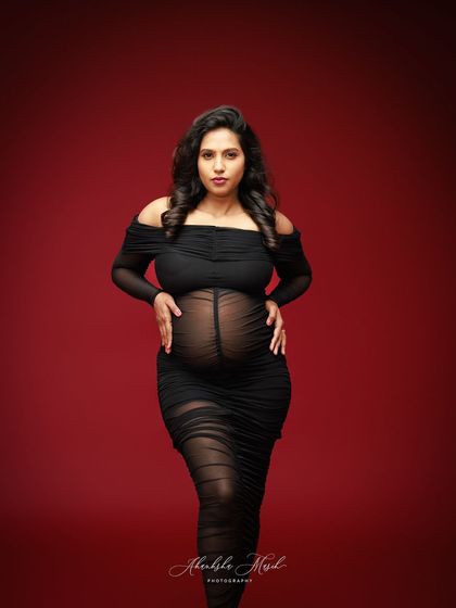 A powerful stance in a sheer black gown against a bold red backdrop, capturing the strength and beauty of the female form during pregnancy.
