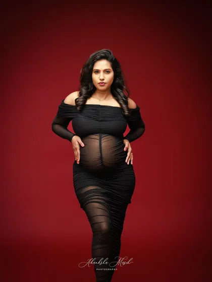 A powerful stance in a sheer black gown against a bold red backdrop, capturing the strength and beauty of the female form during pregnancy.